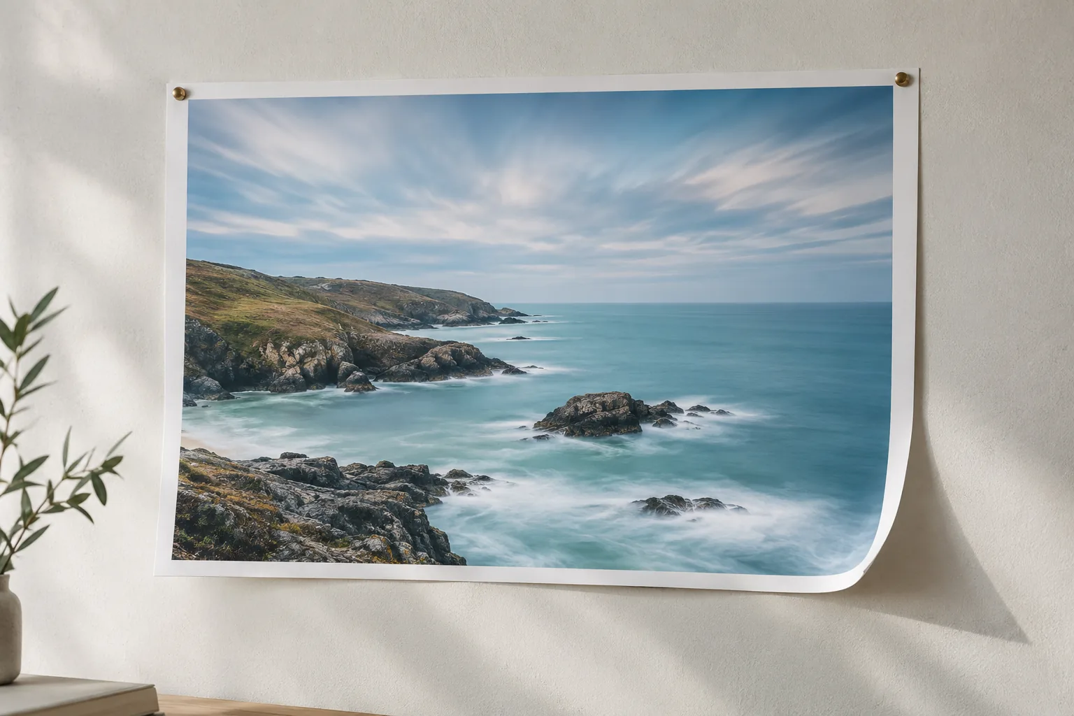 A coastal landscape print pinned to a studio wall with long-exposure clouds and waves inside the frame
